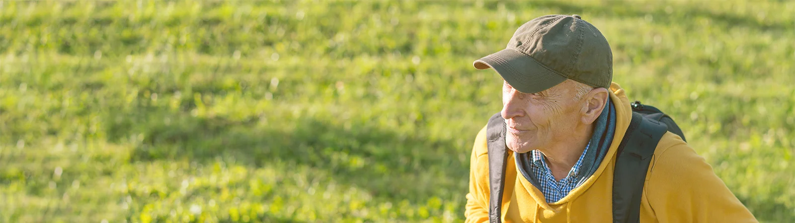 Senior man with backpack hiking outdoors in nature, wearing yellow hoodie and cap, embracing active aging
